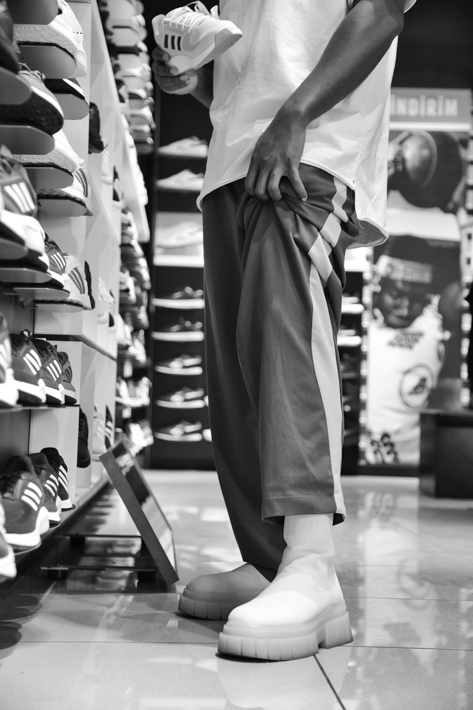 Shopper inspects a white sneaker inside a footwear store.