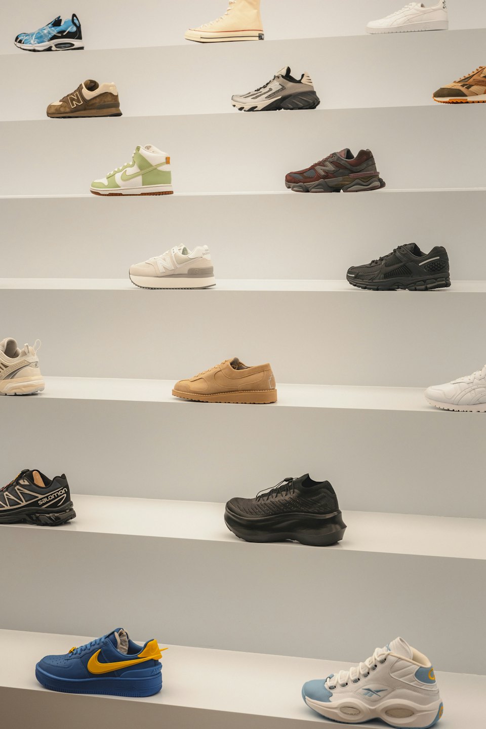 Contemporary sneakers and casual shoes are arranged on white shelves.